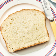 A slice of homemade white bread on a plate with a small dish of butter and a vintage butter knife nearby.