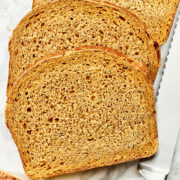A loaf of sliced oatmeal molasses bread on a board with a serrated bread knife nearby.