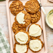 A pink tray of carrot cake cookies, some topped with cream cheese frosting.