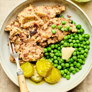 A bowl of Newfoundland-style corned beef hash with peas and mustard pickles on the side.