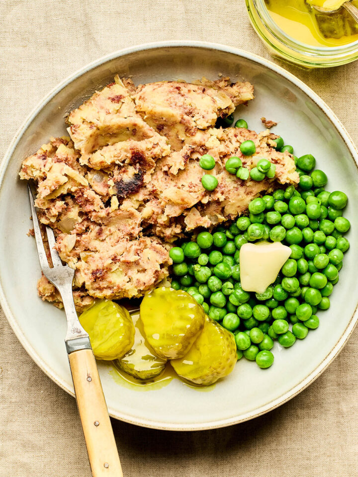 A bowl of Newfoundland-style corned beef hash with peas and mustard pickles on the side.