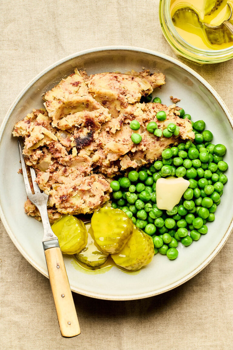A bowl of Newfoundland-style corned beef hash with peas and mustard pickles on the side.