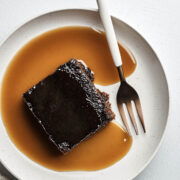 A slice of old-fashioned gingerbread cake topped with brandy sauce on a plate with a fork.
