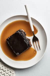 A slice of old-fashioned gingerbread cake topped with brandy sauce on a plate with a fork.