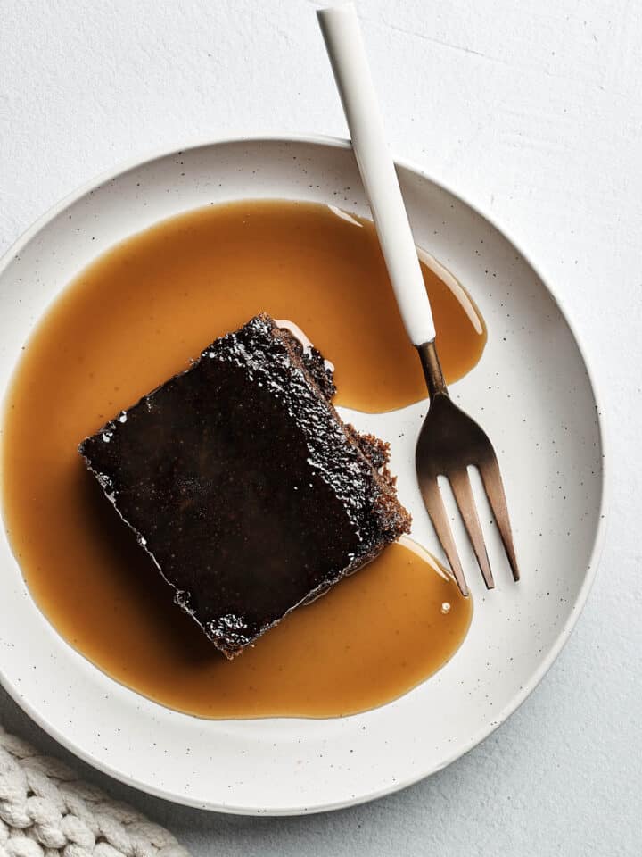 A slice of old-fashioned gingerbread cake topped with brandy sauce on a plate with a fork.