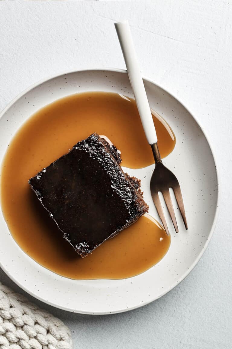 A slice of old-fashioned gingerbread cake topped with brandy sauce on a plate with a fork.