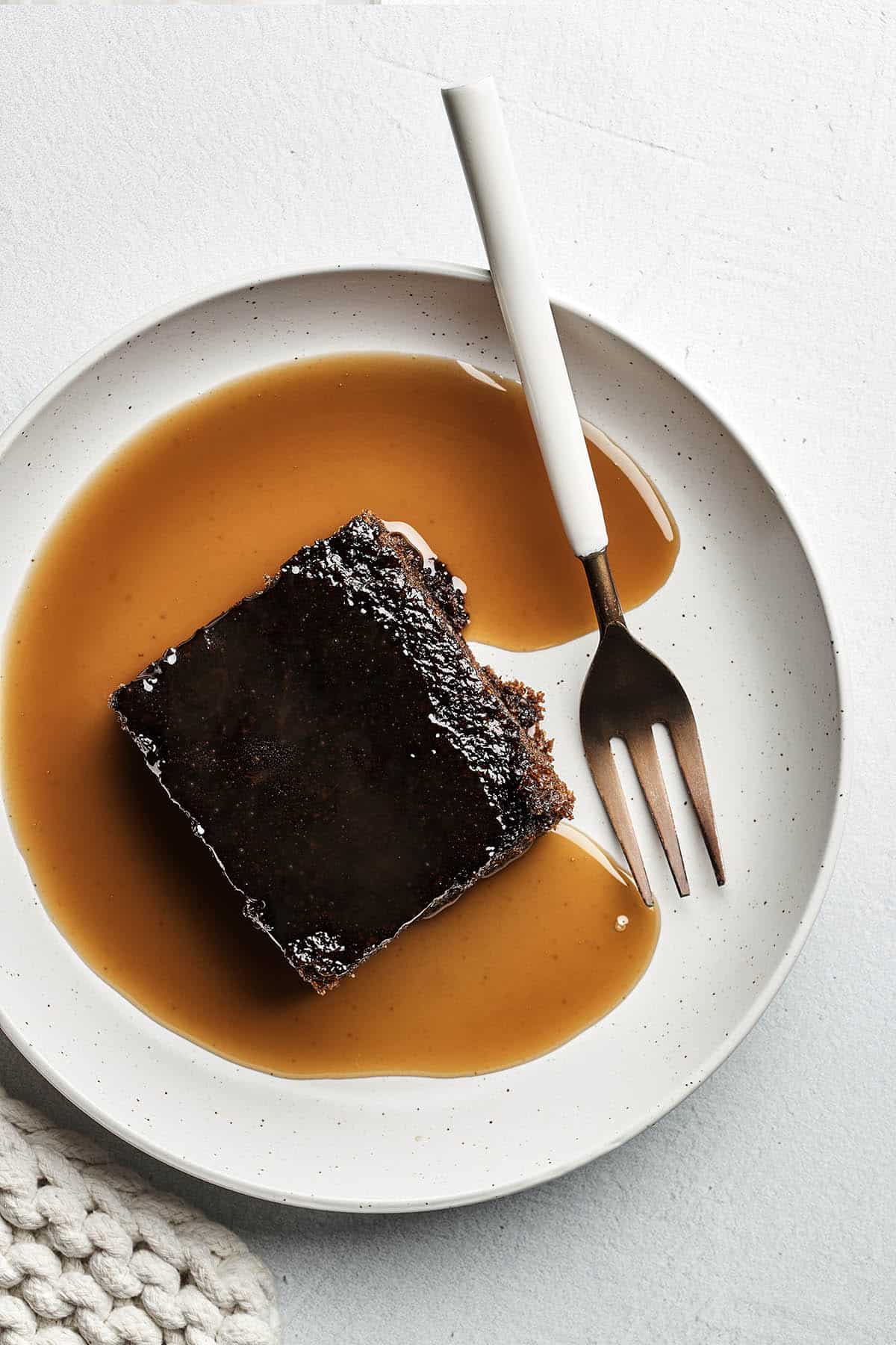 A slice of old-fashioned gingerbread cake topped with brandy sauce on a plate with a fork.