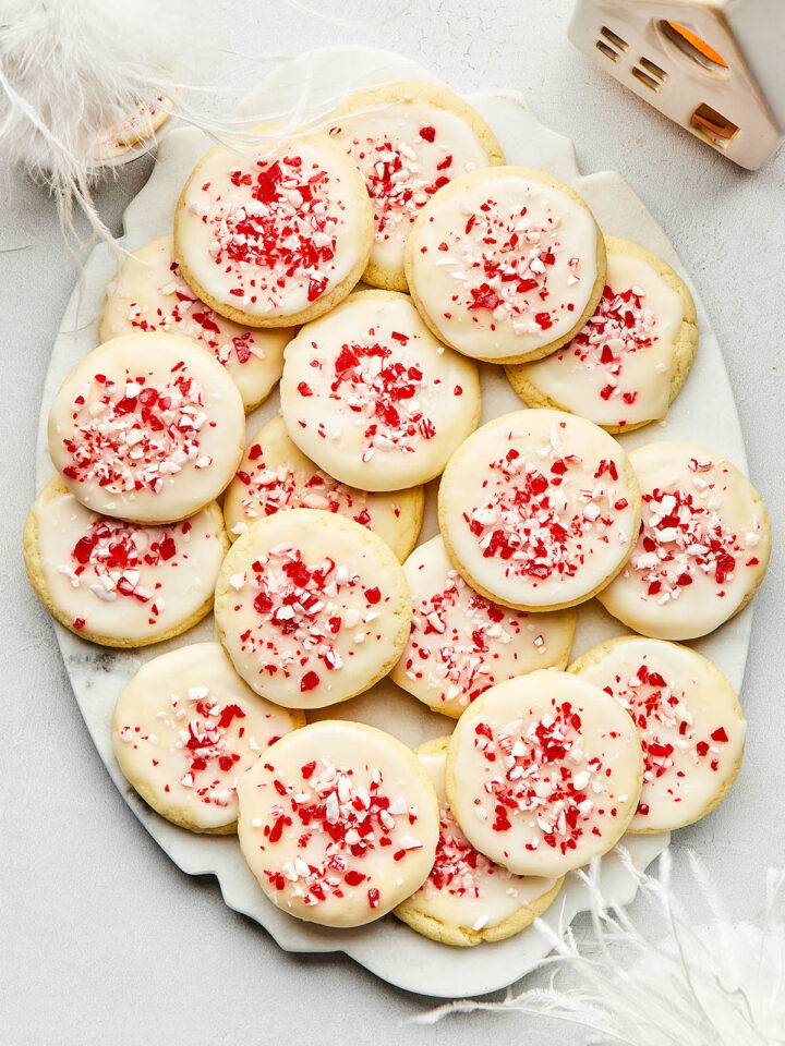 An oval marble platter of peppermint sugar cookies topped with a simple powdered sugar glaze and crushed candy canes.
