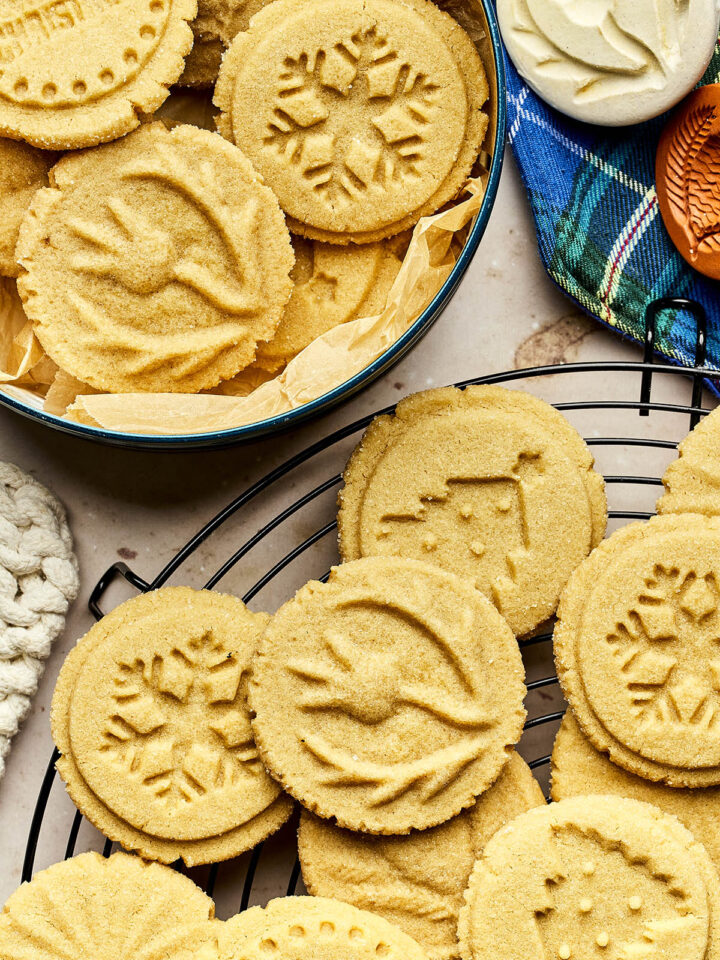 Brown sugar shortbread cookies stamped with various designs arranged in a tin and on a cooling rack.