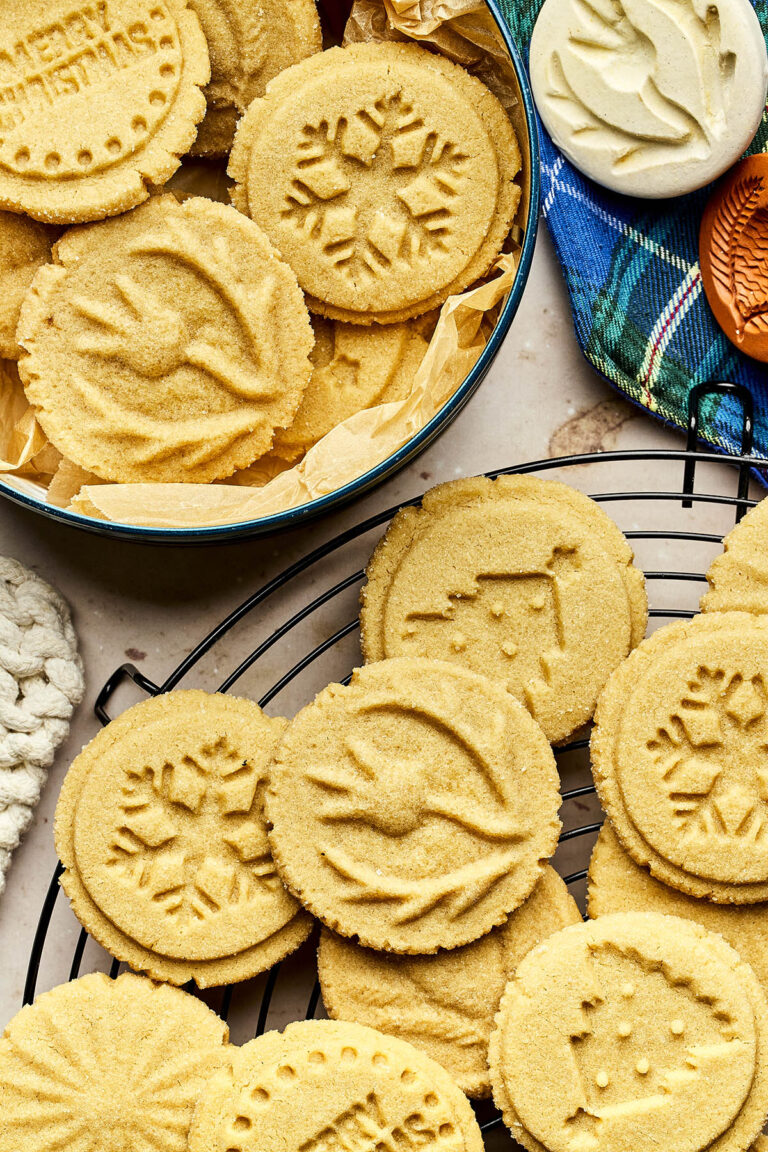 Brown sugar shortbread cookies stamped with various designs arranged in a tin and on a cooling rack.