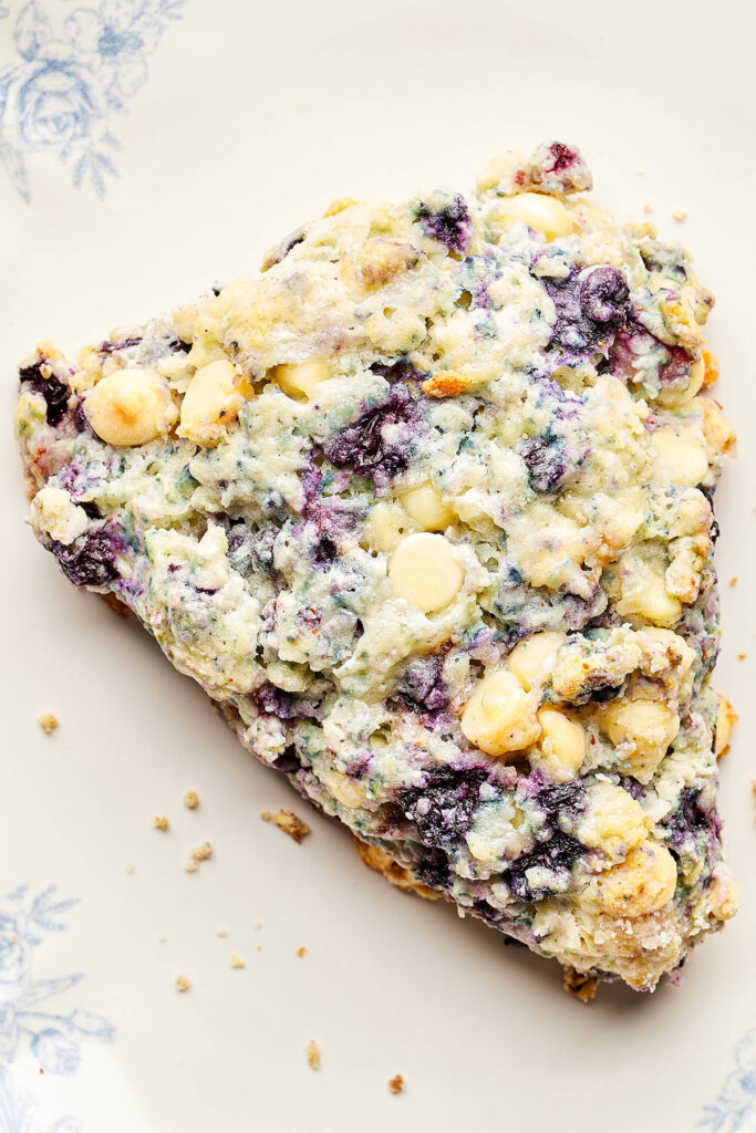 One out of a batch of blueberry white chocolate scones on a blue and white plate.