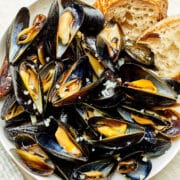A bowl of mussels in white wine sauce with sourdough bread tucked in at the edge of the bowl.