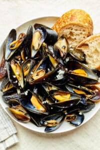 A bowl of mussels in white wine sauce with sourdough bread tucked in at the edge of the bowl.