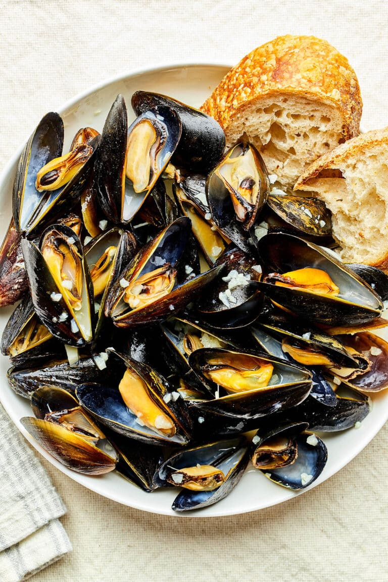A bowl of mussels in white wine sauce with sourdough bread tucked in at the edge of the bowl.