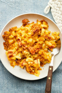 A bowl of lobster mac and cheese on a blue tablecloth.