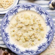 A bowl of my Mum's clam chowder (using canned clams) on a table with saltine crackers, butter, a photo of me and my Mum, and her original recipe card from the 1970s nearby.