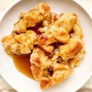 Old-fashioned bread pudding with rum sauce and raisins served in a white bowl.