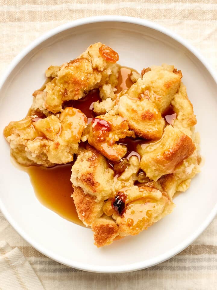 Old-fashioned bread pudding with rum sauce and raisins served in a white bowl.