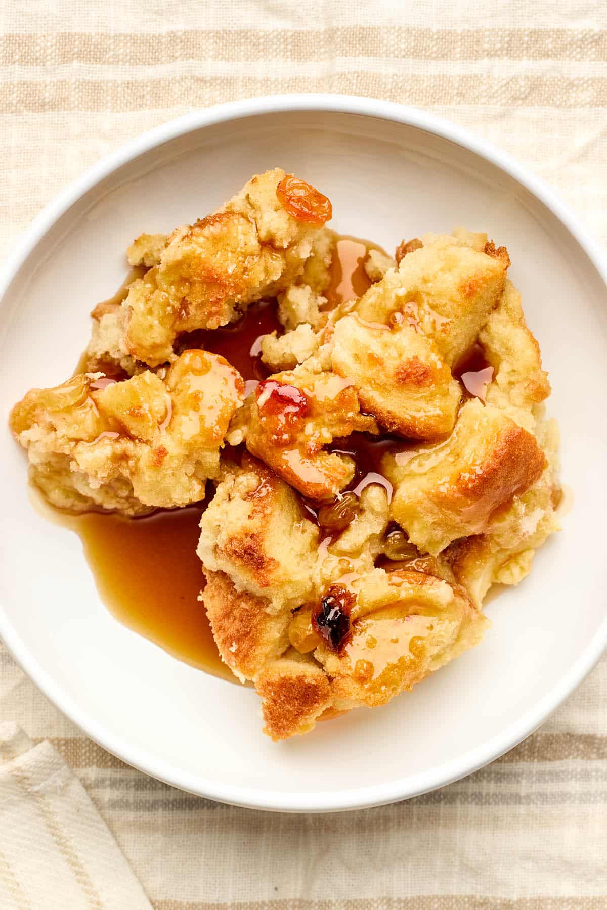 Old-fashioned bread pudding with rum sauce and raisins served in a white bowl.