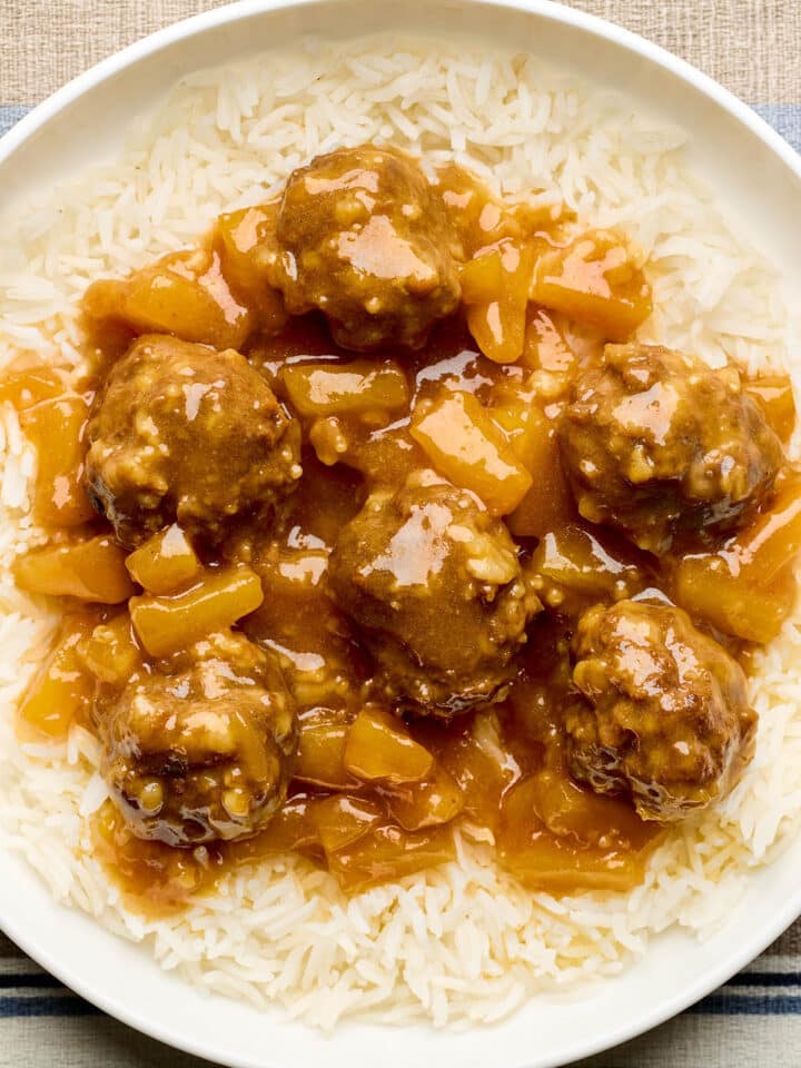 A bowl of sweet and sour beef meatballs with pineapple in a tangy sauce, served over basmati rice.