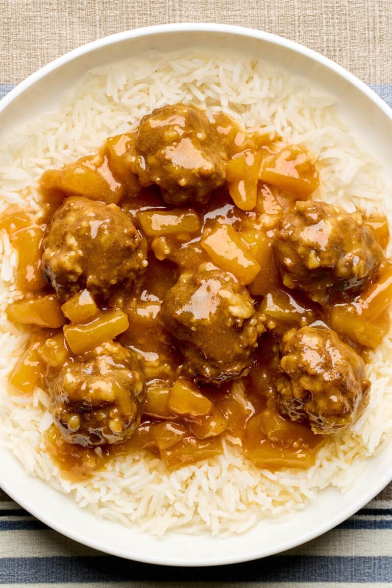 A bowl of sweet and sour beef meatballs with pineapple in a tangy sauce, served over basmati rice.