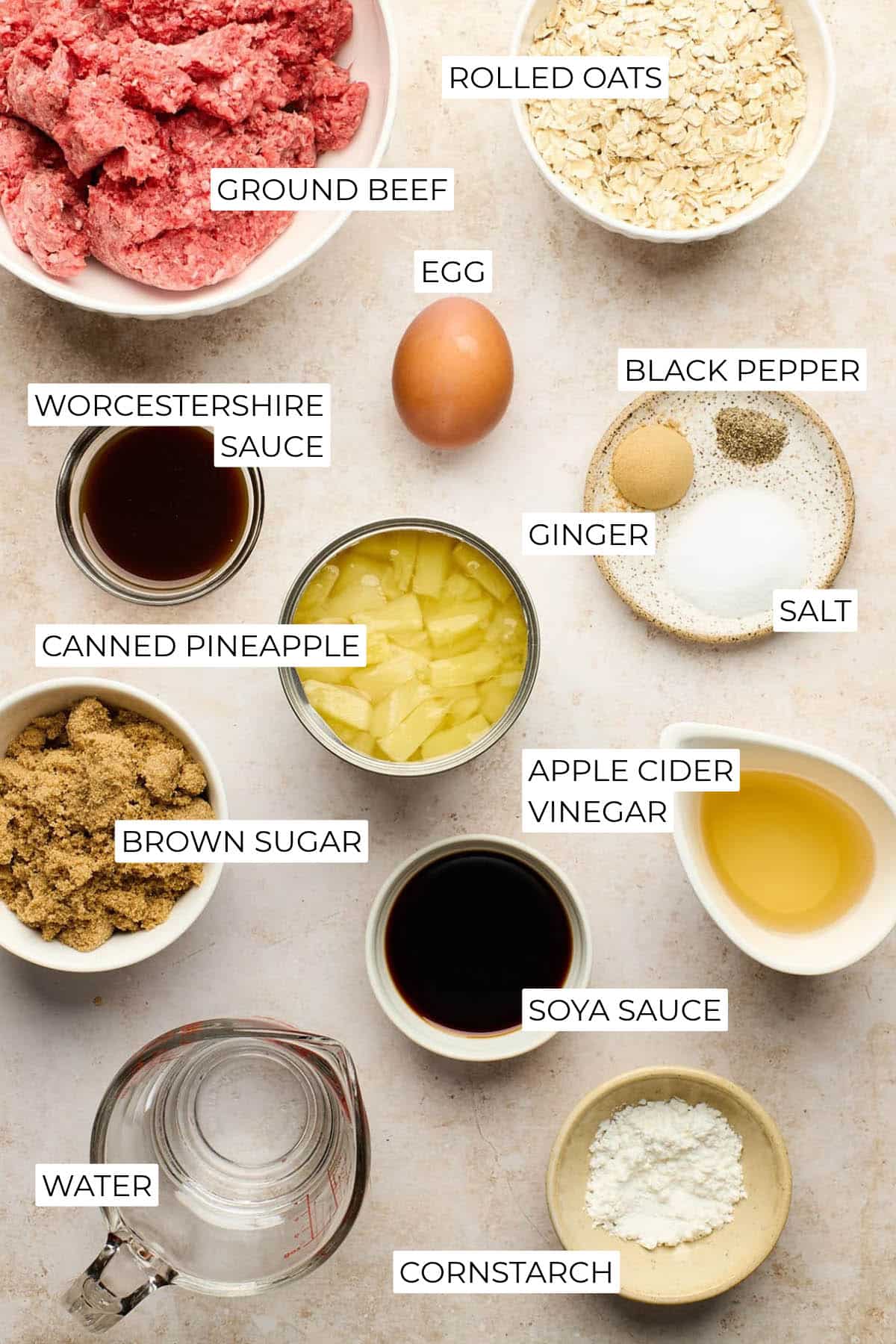 Overhead view of ground beef, rolled oats, egg, seasonings, canned pineapple, brown sugar, vinegar, soya sauce, and cornstarch.